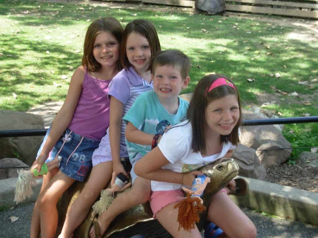 Four kids sitting on a brass turtle at the zoo.